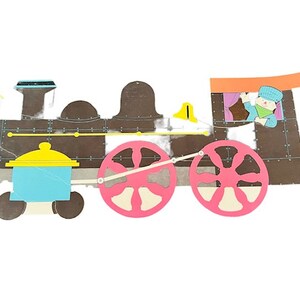 May include: A colorful paper craft train with a brown engine, pink wheels, and a yellow and blue box car. A cartoon character is peeking out of the window of the box car.