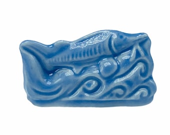 May include: A light blue ceramic figurine of a fish swimming in a wave pattern.