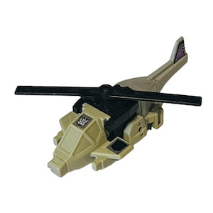 May include: A tan and black toy helicopter with a black rotor and tail fin. The toy has a purple accent on the tail and a logo on the side. The toy is a collectible item.