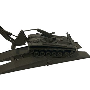 Op de afbeelding: Een donkergroene speelgoedtank met een gedetailleerd ontwerp, met een draaiende geschutskoepel en rupsbanden. De tank staat op een donkergroen platform met hellingen, wat wijst op een militaire voertuigdrager. De algehele esthetiek is realistisch.