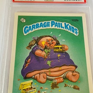 Puede incluir: Una tarjeta de intercambio de Garbage Pail Kids con un personaje de dibujos animados llamado Large Marge. Es un beb&eacute; grande y regordete con un vestido morado y la cara sucia. Est&aacute; sentada en un inodoro con una lata de cola y una caja de caramelos cerca. La tarjeta es verde y tiene el texto "Garbage Pail Kids" y "Large Marge" en ella.
