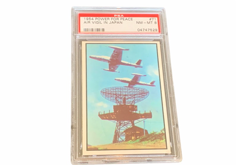 May include: A vintage trading card featuring a color illustration of a radar station with three airplanes flying overhead. The card is graded NM-MT 8 by PSA and has the text "1954 POWER FOR PEACE AIR VIGIL IN JAPAN #71 04747529".