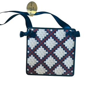 May include: A small, square, blue and red patterned handbag with a navy blue strap and a gold tag that says "The Ashley Road".
