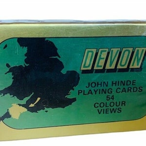 Può includere: Una scatola dorata di carte da gioco John Hinde con uno sfondo verde che presenta una mappa del Regno Unito. La scatola dice "Devon" in grandi lettere dorate e "54 Colour Views" in lettere dorate più piccole.