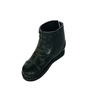 Puede incluir: Una bota de goma negra con cordones. La bota está desgastada y tiene una superficie texturizada.