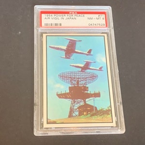 May include: A vintage trading card featuring a photograph of a radar station with two fighter jets flying overhead. The card is titled "1954 Power for Peace Air Vigil in Japan" and is numbered #71. The card is graded NM-MT 8 and has the number 04747528 printed on it.
