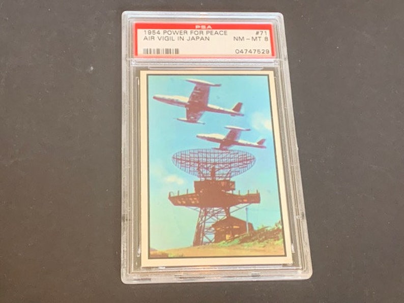 May include: A vintage trading card featuring a photograph of a radar station with two fighter jets flying overhead. The card is titled "1954 Power for Peace Air Vigil in Japan" and is numbered #71. The card is graded NM-MT 8 and has the number 04747528 printed on it.