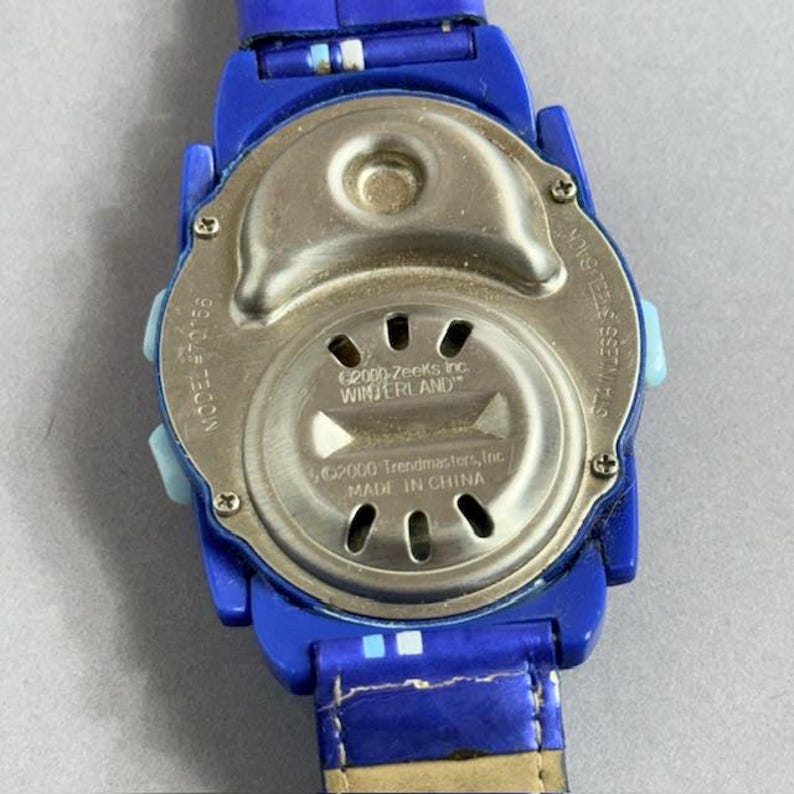 Puede incluir: Un reloj de pulsera azul con una correa azul. La esfera del reloj es plateada con el texto "&copy;2000-Zeeks Inc. WINTERLAND" y "&copy;2000 Trendmasters, Inc. MADE IN CHINA". La parte trasera del reloj es de acero inoxidable. Modelo #70156.
