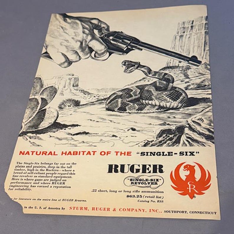 May include: Vintage advertisement for the Ruger Single-Six revolver. The image features a hand holding the revolver above a coiled rattlesnake in a desert landscape. The ad includes the Ruger logo and text about the revolver.