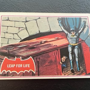 Könnte beinhalten: Eine Vintage-Comic-Sammelkarte mit Batman, der aus einem Waggon eines Zuges springt. Die Karte hat ein rotes Fledermauslogo mit dem Text "Leap for Life".