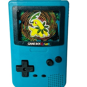 Pode incluir: Um console de videogame portátil Game Boy Color azul turquesa com uma tela em preto e branco mostrando um personagem Pokémon verde e amarelo. O console possui um direcional preto, dois botões pretos rotulados como A e B, e o texto "GAME BOY.COLOR" e "Nintendo" impresso na frente.
