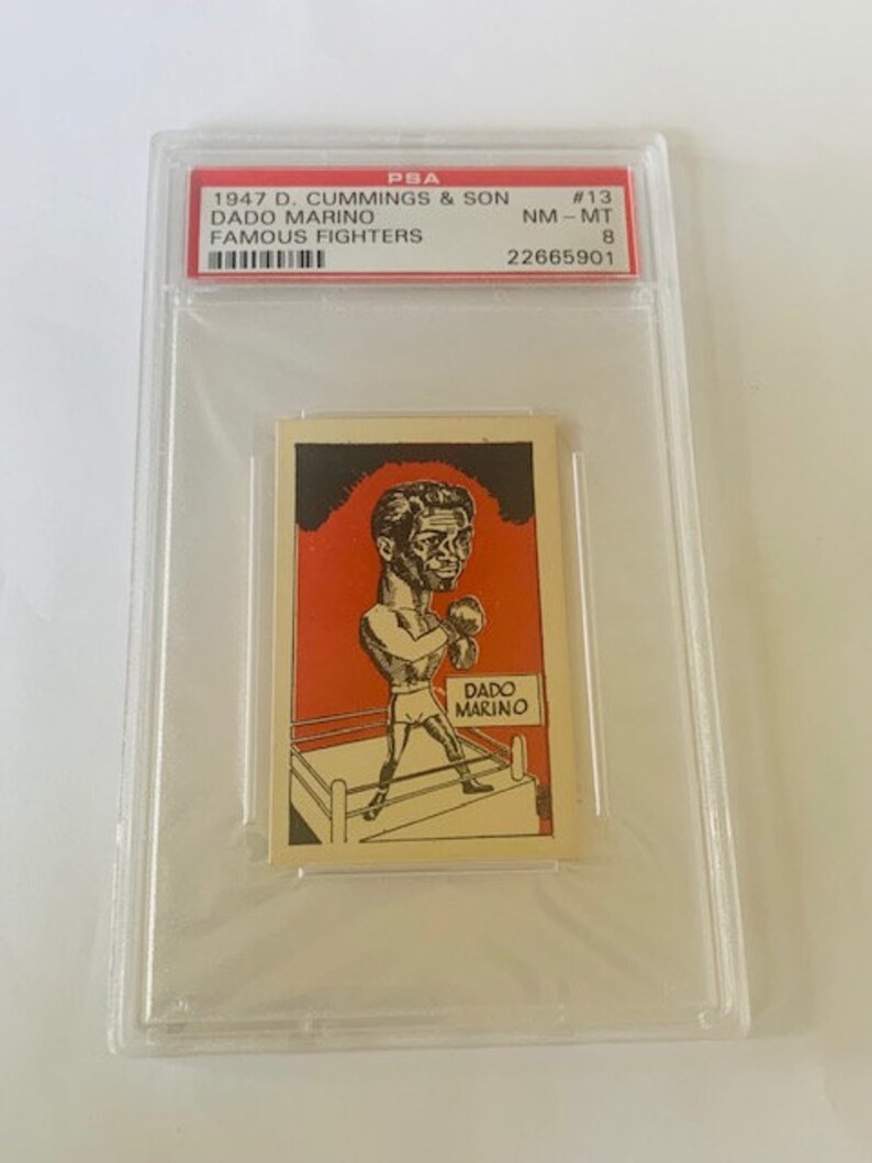 May include: A vintage trading card featuring a black and white illustration of a boxer in a boxing ring. The card is from the 1947 D. Cummings & Son Famous Fighters series and features Dado Marino. The card is graded NM-MT 8 by PSA and has the number 22665901.