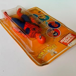 May include: A red and blue Spider-Man action figure in a plastic blister pack. The packaging features the words "SUPER HEROES" and "SPIDER-MAN" in yellow and black lettering.