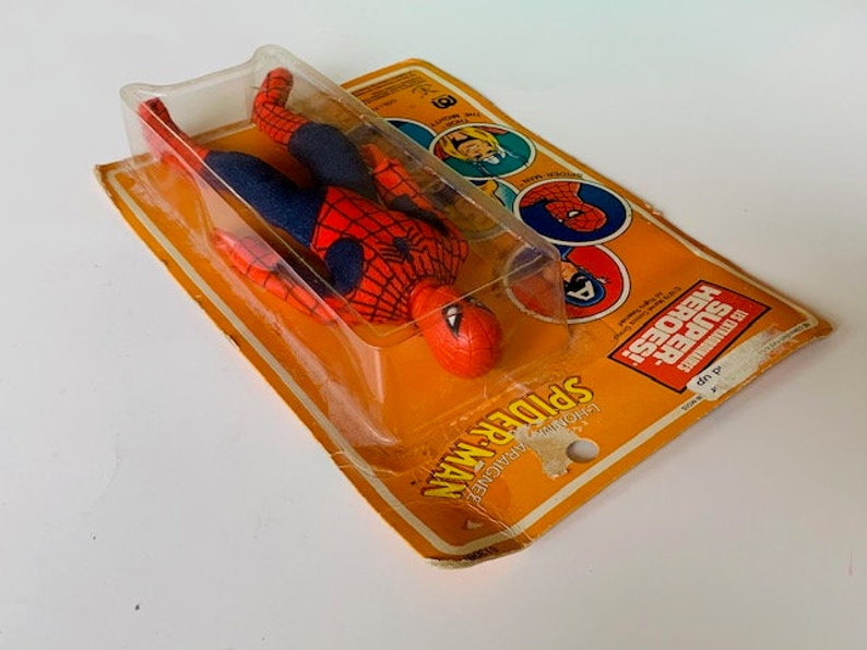 May include: A red and blue Spider-Man action figure in a plastic blister pack. The packaging features the words "SUPER HEROES" and "SPIDER-MAN" in yellow and black lettering.