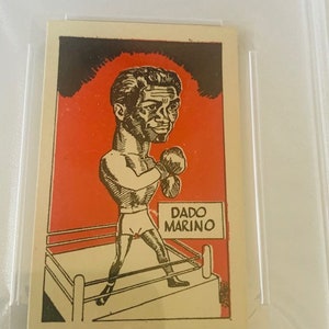 May include: A black and white cartoon illustration of a boxer in a boxing ring. The boxer is wearing boxing gloves and shorts. The text "DADO MARINO" is printed on a white rectangle in the upper right corner of the image.