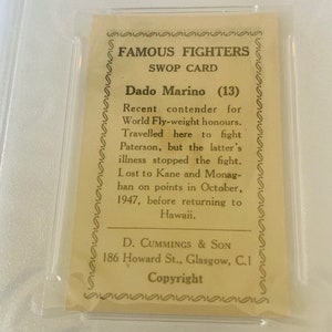 May include: A vintage trading card featuring a black and white photo of a boxer. The card is titled "Famous Fighters Swop Card" and features the text "Dado Marino (13)" and a biography of the boxer.