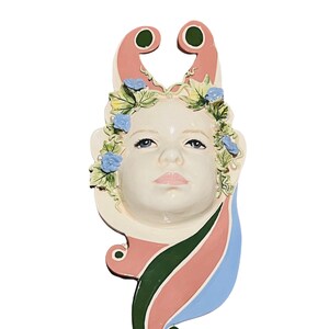 Puede incluir: Una escultura de pared de cerámica de una cara con una corona floral y un diseño de espiral rosa, verde y azul.