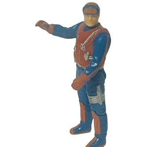 Puede incluir: Una figura de acción azul y naranja con un chaleco rojo y gafas. La figura lleva un mono azul con detalles naranjas y un cinturón plateado.