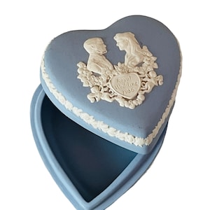 Op de afbeelding: Een blauwe hartvormige sieradendoos met een wit ontwerp van een stel en de tekst "Royal Wedding 1986".