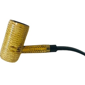 May include: A yellow corncob pipe with a black stem. The bowl of the pipe is made of a natural material and has a textured surface.