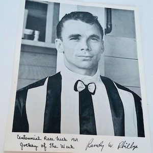 May include: Black and white photo of a jockey wearing a striped uniform and a bow tie. The photo is signed "Randy W. Philly" and includes the text "Centennial Race Track 1969 Jockey of the Week".