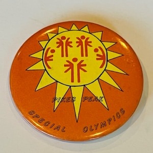 May include: Orange and yellow button with a sun design and the text "Pikes Peak Special Olympics".