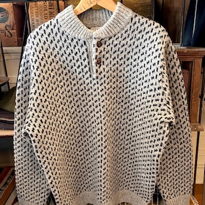May include: A gray and black patterned sweater with a button-up collar. The sweater is hanging on a wooden hanger. The sweater has a textured design and a ribbed collar and cuffs.