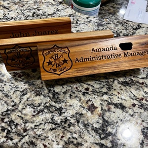 May include: Two wooden desk nameplates with the Corpus Christi Fire Department logo and the names "John Juarez" and "Amanda Administrative Manager".