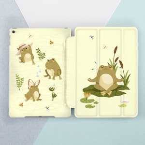 Puede incluir: Una funda de teléfono amarilla y blanca con un diseño de rana. La funda tiene una rana meditando en un nenúfar, una rana con un sombrero y una rana con alas de mariposa. La funda está hecha de un material plástico duro.