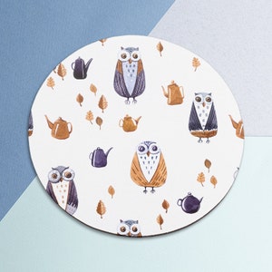 Puede incluir: Posavasos redondo blanco con un patrón repetido de búhos y teteras. Los búhos son marrones, morados y grises con ojos grandes. Las teteras son marrones, moradas y grises. El fondo es blanco con hojas marrones.