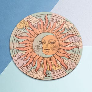 May include: Round coaster featuring a celestial design with a sun and moon face, surrounded by clouds. The sun has orange rays and a peach-colored face, while the moon is light blue. The background is a light green with a dotted border.