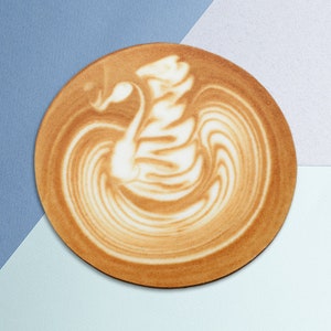 Puede incluir: Un primer plano de un latte con un diseño de cisne en la espuma. El latte está en una taza blanca y está sobre un fondo azul y blanco.
