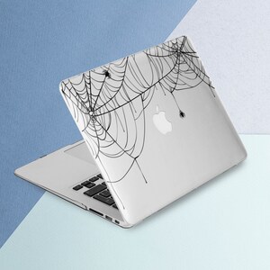 May include: A white laptop computer with a black spiderweb design on the lid. The design features several spiders in the web.