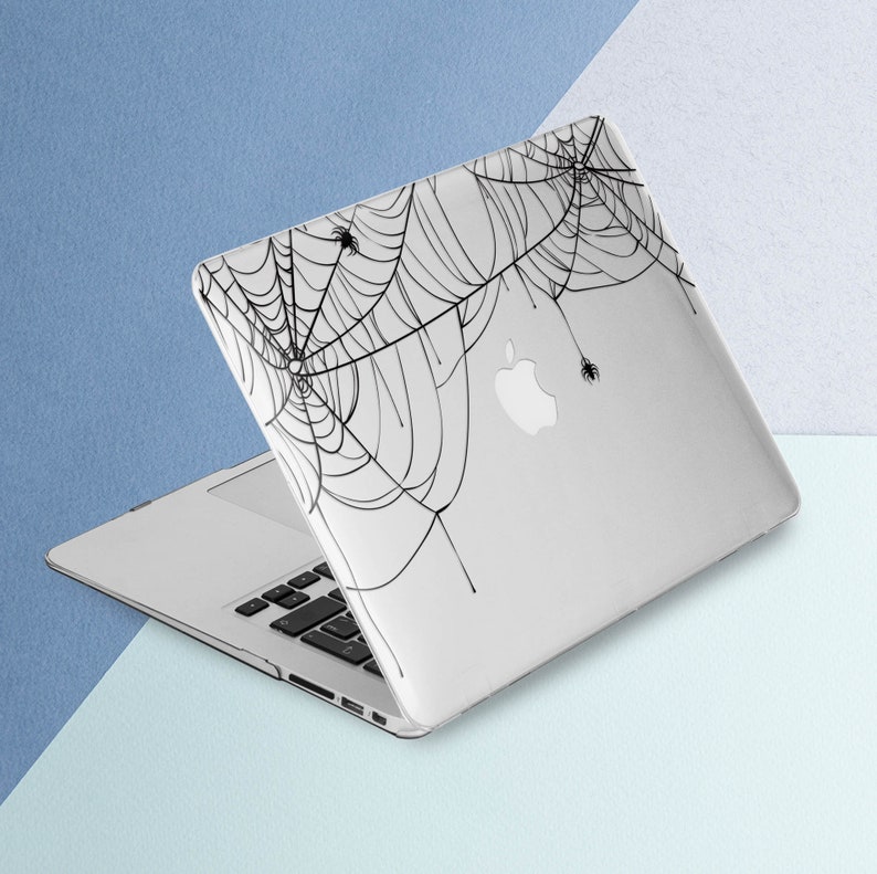 May include: A white laptop computer with a black spiderweb design on the lid. The design features several spiders in the web.