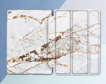 May include: A white and gold marble iPad case with a folding cover. The case is made of a hard plastic material and has a smooth finish.