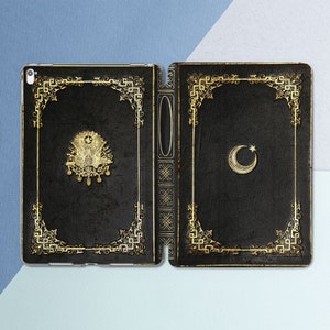Puede incluir: Una funda para iPad de cuero negro con un diseño dorado. La funda tiene un borde decorativo con una luna creciente y una estrella en el lado derecho y un emblema nacional turco en el lado izquierdo.