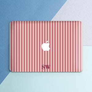 May include: A laptop case with a pink and white striped pattern. The Apple logo is centered, with the initials "SW" below it. The case is on a background of blue and white.