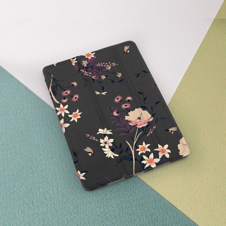 May include: A black tablet case with a floral pattern featuring pink, white, and yellow flowers and bees. The case has a textured surface.