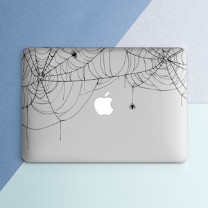 May include: A gray laptop computer with a black spiderweb design on the lid. The design features several spiders and dripping strands of web.