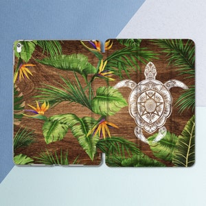 Puede incluir: Una funda para teléfono con estampado de madera con una ilustración blanca detallada de una tortuga con un diseño de mandala. El fondo presenta hojas tropicales verdes y flores amarillas de ave del paraíso.
