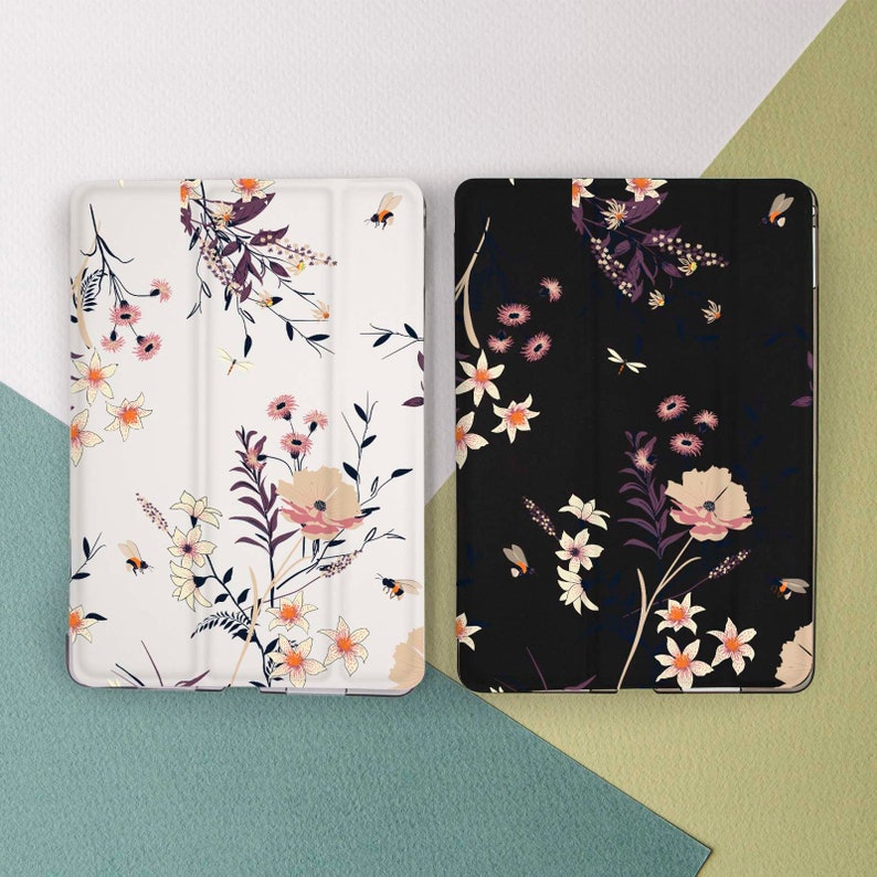 May include: Two tablet cases with floral patterns. One case is white with a floral pattern in shades of pink, white, and brown. The other case is black with a floral pattern in shades of pink, white, and brown.