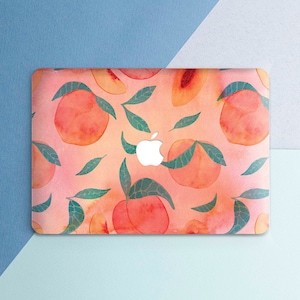 Puede incluir: Una piel de portátil rosa con un patrón de acuarela de melocotones y hojas. La piel tiene un logotipo de Apple blanco en el centro.
