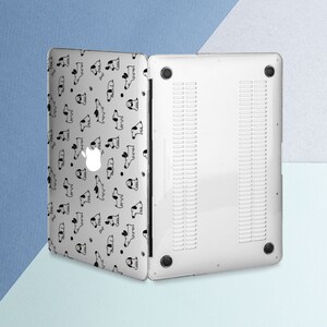 Puede incluir: Una funda transparente para port&aacute;til con un patr&oacute;n repetido de ilustraciones de perros en blanco y negro. La funda est&aacute; abierta, revelando el logotipo plateado de Apple del port&aacute;til. La parte inferior de la funda es blanca con ranuras de ventilaci&oacute;n y patas de goma negras.