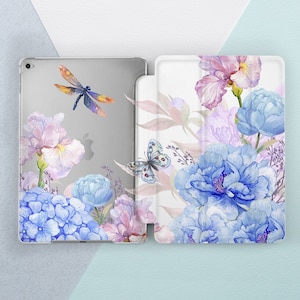 Puede incluir: Una funda de teléfono blanca con un diseño floral con flores azules, moradas y rosas, una mariposa y una libélula.