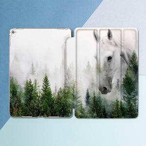 Op de afbeelding: Het hoofd van een wit paard is gedeeltelijk zichtbaar in een mistige bosscène. Het paardenhoofd bevindt zich op de voorgrond en het bos op de achtergrond. Het bos bestaat uit hoge, groene dennenbomen. De afbeelding is een ontwerp voor een telefoonhoesje.