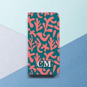 May include: A teal phone case featuring a coral-colored abstract pattern. The design includes organic shapes resembling coral or plant life. The initials "CM" are displayed in a white oval at the bottom. The case has a smooth finish.