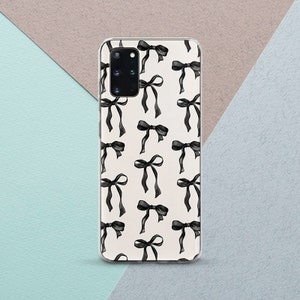 May include: A clear phone case with a repeating pattern of black bows on a white background. The bows have long, flowing ribbons. The case is displayed on a light blue, grey, and tan surface.