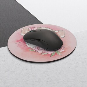 May include: A round pink mouse pad with a watercolor illustration of a mouse's face with pink flowers. A black computer mouse is on top of the mouse pad.