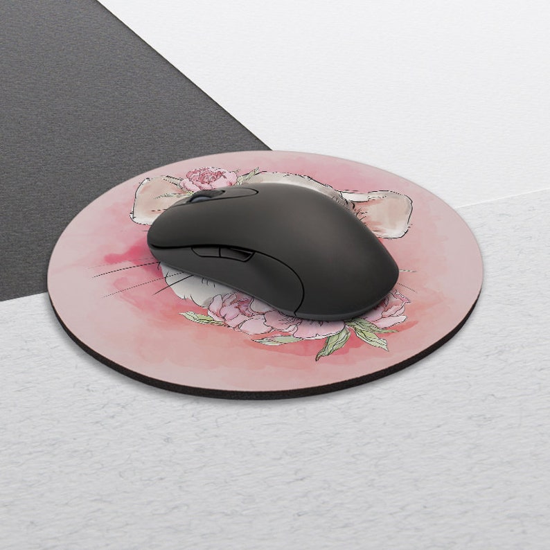 May include: A round pink mouse pad with a watercolor illustration of a mouse's face with pink flowers. A black computer mouse is on top of the mouse pad.