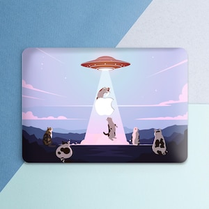 May include: Laptop skin featuring a whimsical illustration of cats being abducted by a UFO. The scene includes a red and orange spaceship, a white Apple logo, and cats in various poses against a purple and blue landscape.